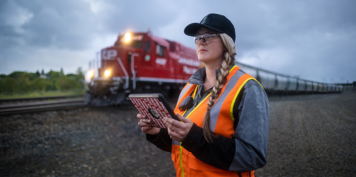 Une cheminote regarde les voies en tenant un iPad pendant qu’un train passe